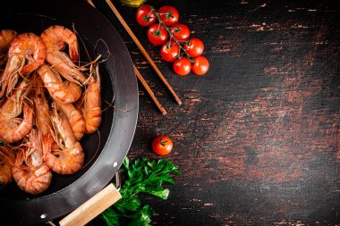 Cooked shrimp in a saucepan with parsley and tomatoes. On rustic dark background. High quality photo