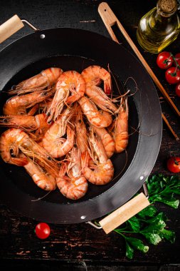 Cooked shrimp in a saucepan with parsley and tomatoes. On rustic dark background. High quality photo