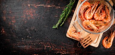 Boiled shrimp in a colander with a sprig of rosemary. Against a dark background. High quality photo