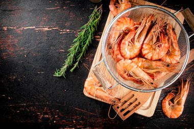Boiled shrimp in a colander with a sprig of rosemary. Against a dark background. High quality photo