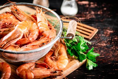 Boiled shrimp in a colander on a cutting board with parsley. Against a dark background. High quality photo