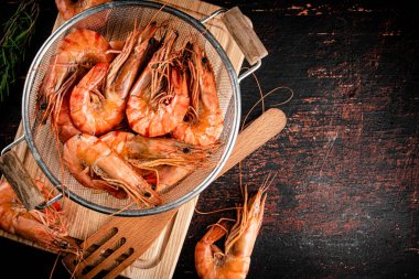 Boiled shrimp in a colander with a sprig of rosemary. Against a dark background. High quality photo