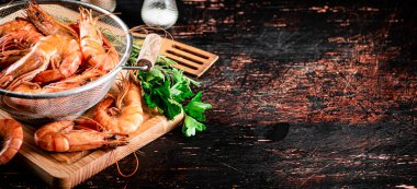 Boiled shrimp in a colander on a cutting board with parsley. Against a dark background. High quality photo