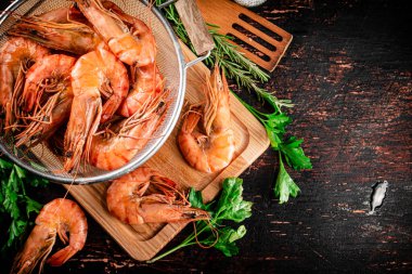 Boiled shrimp in a colander on a cutting board with parsley. Against a dark background. High quality photo