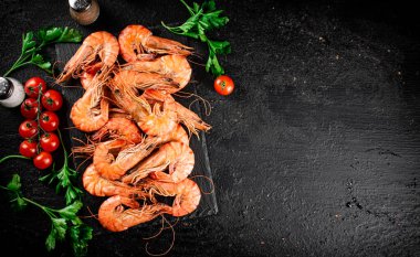 Boiled shrimp on a stone board with tomatoes and parsley. On a black background. High quality photo