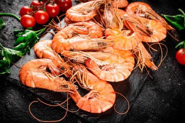 Boiled shrimp on a stone board with tomatoes and parsley. On a black background. High quality photo