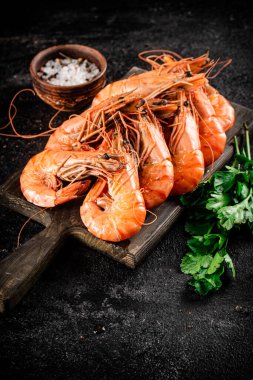 Boiled shrimp on a cutting board with parsley and spices. On a black background. High quality photo