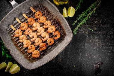 Grilled shrimp on skewers in a frying pan with rosemary and pieces of lime. On a black background. High quality photo