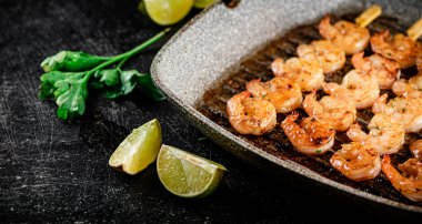Grilled shrimp in a frying pan with parsley and pieces of lime. On a black background. High quality photo
