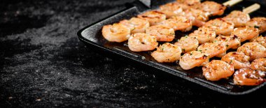 Shrimp on skewers are grilled in a grill pan. On a black background. High quality photo