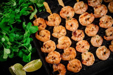 Grilled shrimp in a frying pan with parsley and pieces of lime. On a black background. High quality photo
