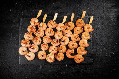 Delicious grilled shrimp on skewers on a stone board. On a black background. High quality photo