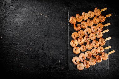 Delicious grilled shrimp on skewers on a stone board. On a black background. High quality photo