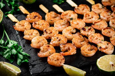 Grilled shrimp on a stone board with parsley and lime. On a black background. High quality photo