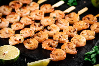Grilled shrimp on a stone board with parsley and lime. On a black background. High quality photo