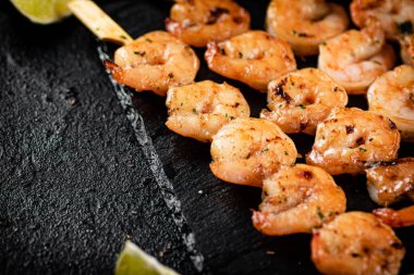 Grilled shrimp on a stone board with pieces of lime. On a black background. High quality photo