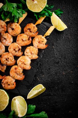 Grilled shrimp on a stone board with parsley and lime. On a black background. High quality photo