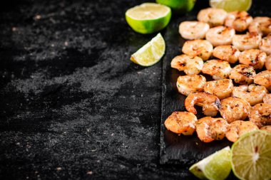 Grilled shrimp on a stone board with pieces of lime. On a black background. High quality photo