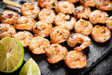 Grilled shrimp on a stone board with pieces of lime. On a black background. High quality photo