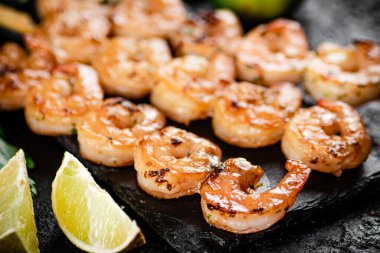 Grilled shrimp on a stone board with pieces of lime. On a black background. High quality photo