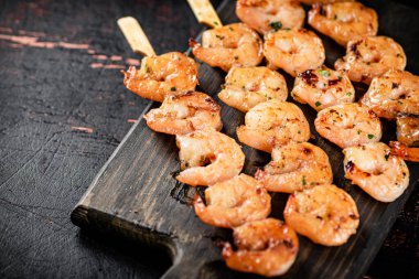 Grilled shrimp on skewers on a cutting board. Against a dark background. High quality photo