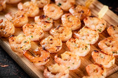 Grilled shrimp on skewers on a cutting board. Against a dark background. High quality photo