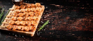 Delicious grilled shrimp on a cutting board with rosemary and spices. On a rustic dark background. High quality photo