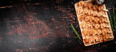 Delicious grilled shrimp on a cutting board with rosemary and spices. On a rustic dark background. High quality photo