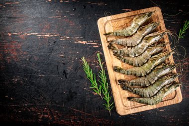 Raw shrimp on a cutting board with rosemary. Against a dark background. High quality photo