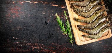 Raw shrimp on a cutting board with rosemary. Against a dark background. High quality photo