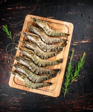 Raw shrimp on a cutting board with rosemary. Against a dark background. High quality photo