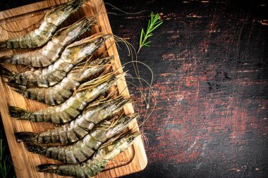 Raw shrimp on a cutting board with rosemary. Against a dark background. High quality photo