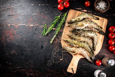 Raw shrimp on a wooden cutting board with tomatoes and spices. Against a dark background. High quality photo