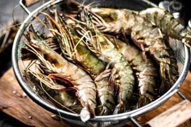 Fresh uncooked shrimp in a colander. On rustic dark background. High quality photo