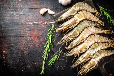 Raw shrimp on a cutting board with rosemary and garlic. Against a dark background. High quality photo