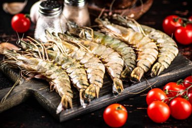Raw shrimp on a cutting board with spices and tomatoes. Against a dark background. High quality photo