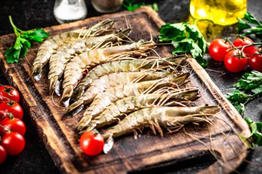 Raw shrimp on a cutting board with parsley and tomatoes. On a black background. High quality photo