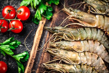 Raw shrimp on a cutting board with parsley and tomatoes. On a black background. High quality photo