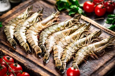 Raw shrimp on a cutting board with parsley and tomatoes. On a black background. High quality photo