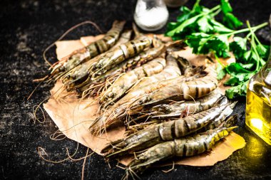 Raw shrimp on paper with spices and parsley. On a black background. High quality photo