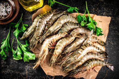 Raw shrimp on paper with spices and parsley. On a black background. High quality photo