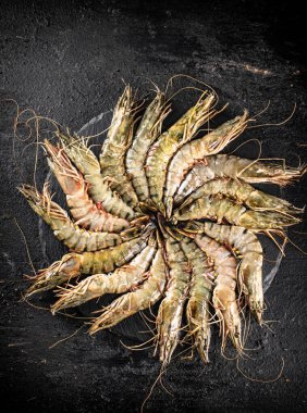 Fresh raw shrimp on a round stone board. On a black background. High quality photo