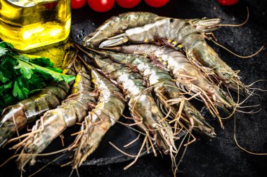 Raw shrimp on a stone board with parsley and tomatoes. On a black background. High quality photo