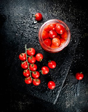 Pickled tomatoes in a jar on a stone board. On a black background. High quality photo