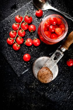 Pickled tomatoes in a jar on a stone board. On a black background. High quality photo