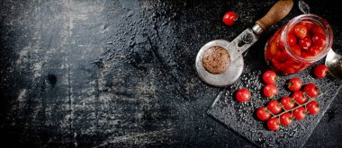 Pickled tomatoes in a jar on a stone board. On a black background. High quality photo