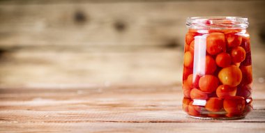 Pickled ripe tomatoes in a glass jar. On a wooden background. High quality photo