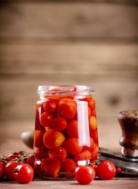 Pickled ripe tomatoes in a glass jar. On a wooden background. High quality photo