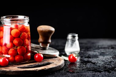 Pickled tomatoes in a glass jar on a cutting board. On a black background. High quality photo