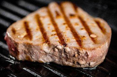 Tuna steak in a grill pan. On a black background. High quality photo